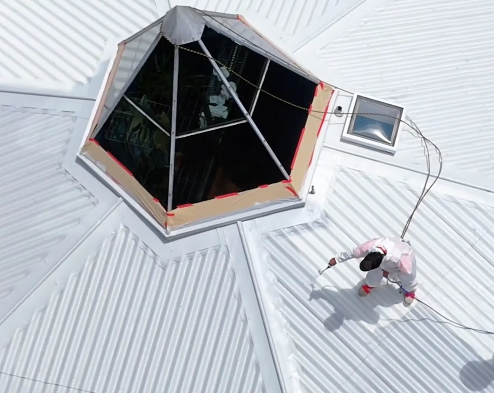 Applicator in protective coveralls spray applying white Noxyde membrane to the Titirangi roof
